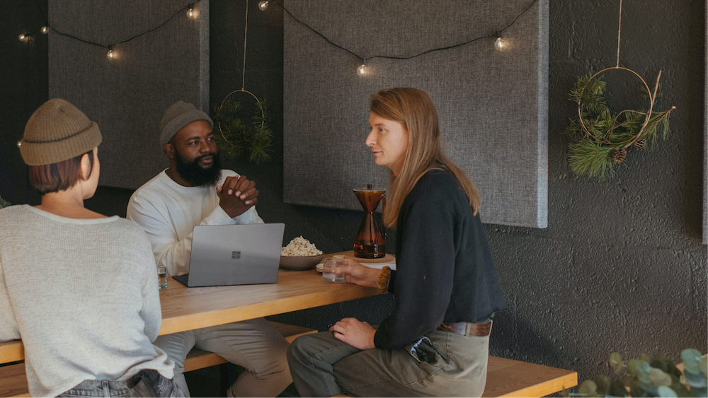 Three people sitting at a table having popcorn and talking. 